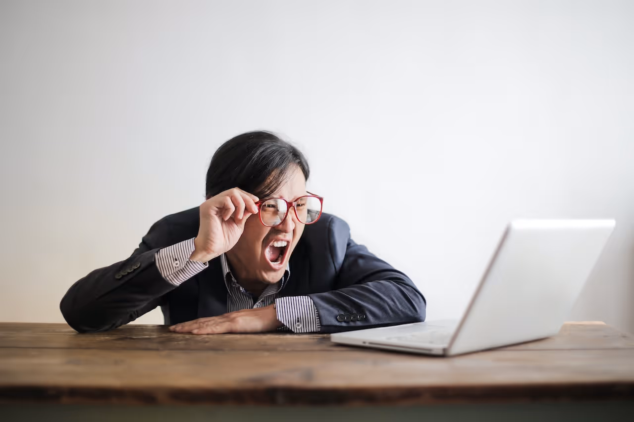 A distressed Asian male angrily shouting in front of his laptop screen