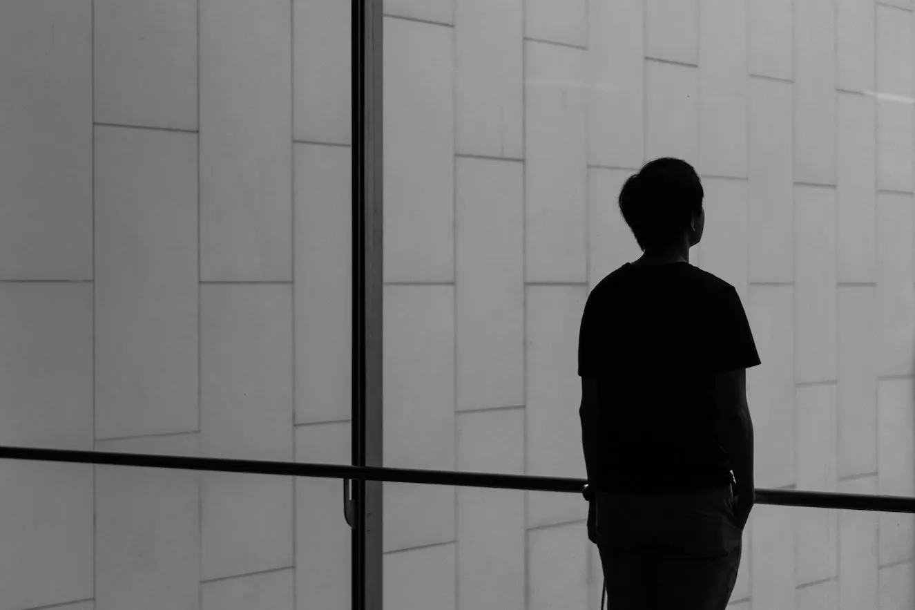A silhouette of a young Asian man looking outside a large window